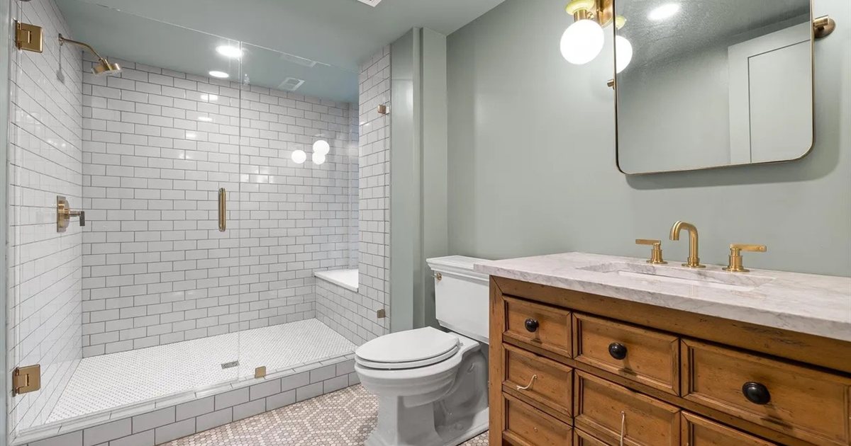 How to clean shower glass: frameless glass shower enclosure with white subway tile and brushed brass hardware in a modern bathroom